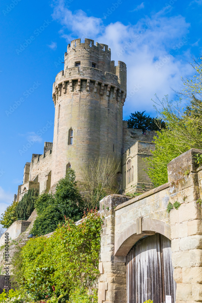 Caesar's Tower part of the dramatic Warwick Castle fortress, with trees and flowers of Mill Garden below, beautiful blue spring sky, April 2017, Warwick, Warwickshire, United Kingdom, UK
