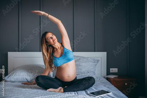 Young pregnant woman exercising on her bed