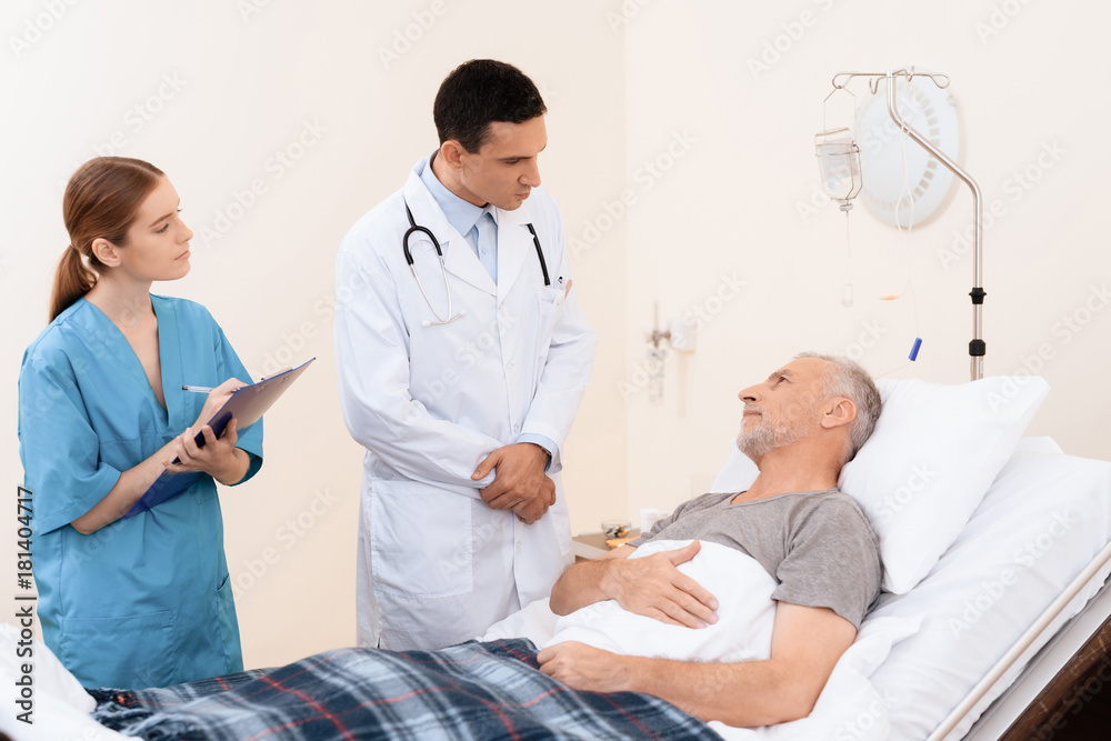 Obraz premium The old man lies on a cot in the medical ward. Next to him is a doctor and a nurse.
