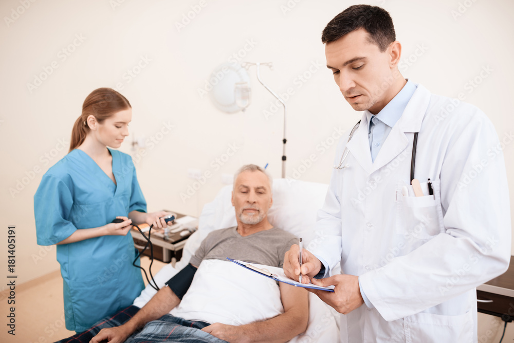 Obraz premium The old man lies on a cot in the medical ward, and next to him there is a doctor and a nurse.