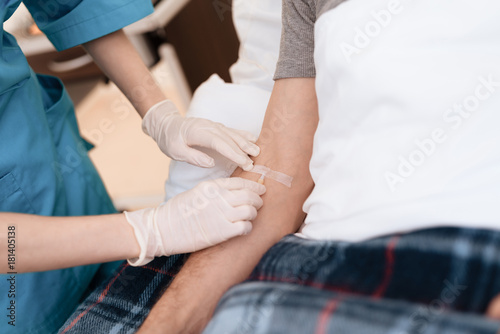 The old man lies on a cot in the medical ward  and the nurse puts him a dropper. She has medical gloves on her hands.