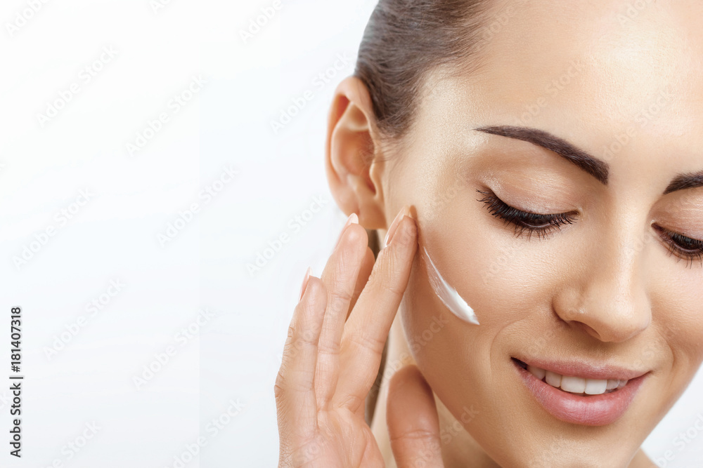 Facial Care. Female Applying Cream and Smiling.Portrait Of  Young Woman With Cosmetic Cream On Skin. Closeup Of Beautiful Girl With Beauty Product On Soft Skin, Natural Makeup Touching Face.