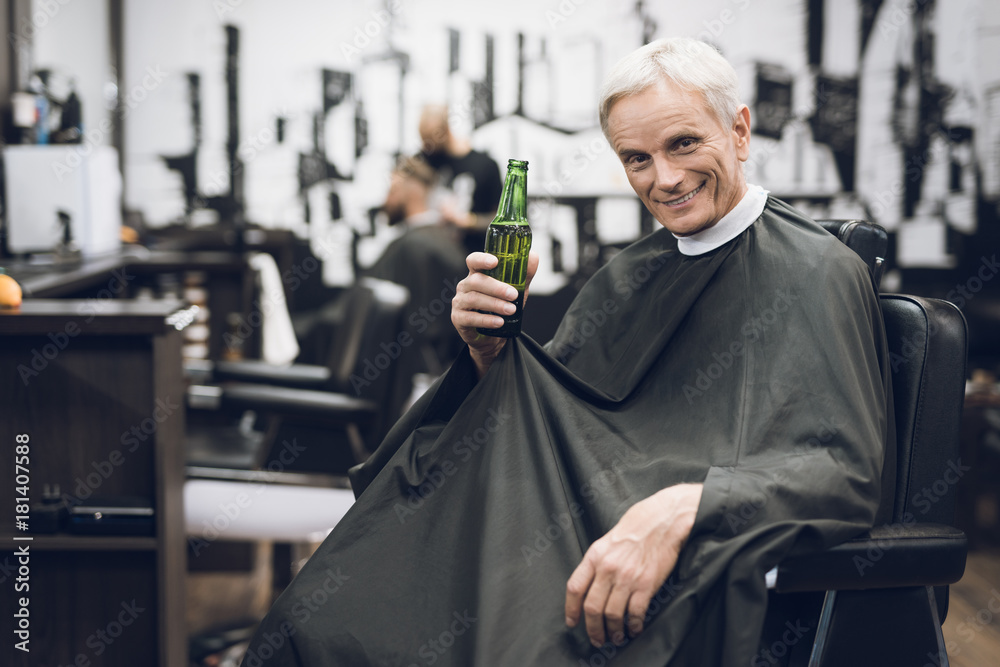 The old man drinks alcohol in the barber's chair in barbershop.
