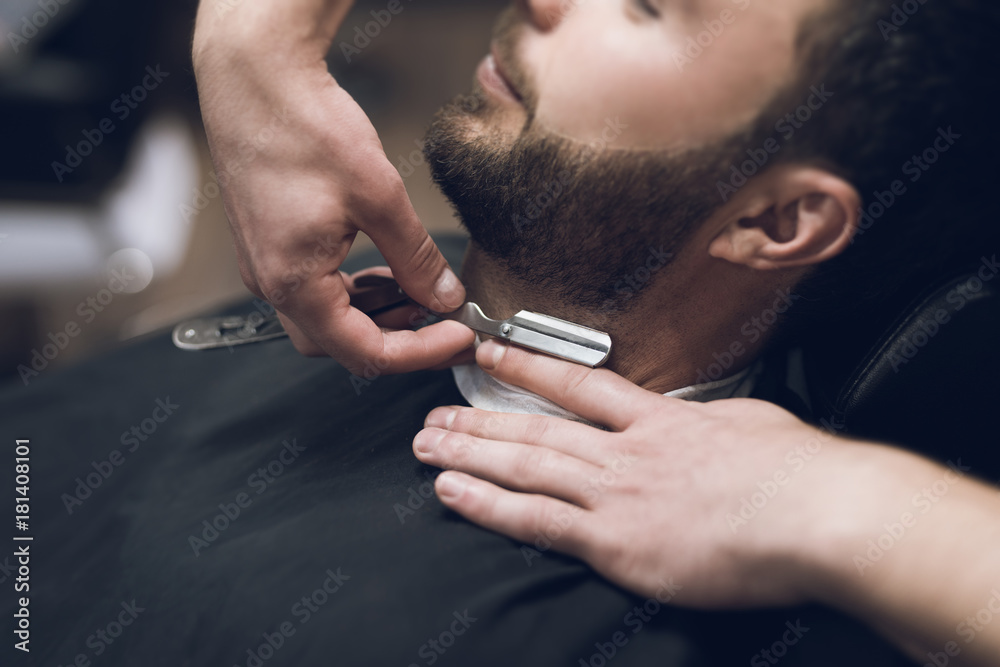 The barber shaves his head, mustache and beard to the man in the barbershop.