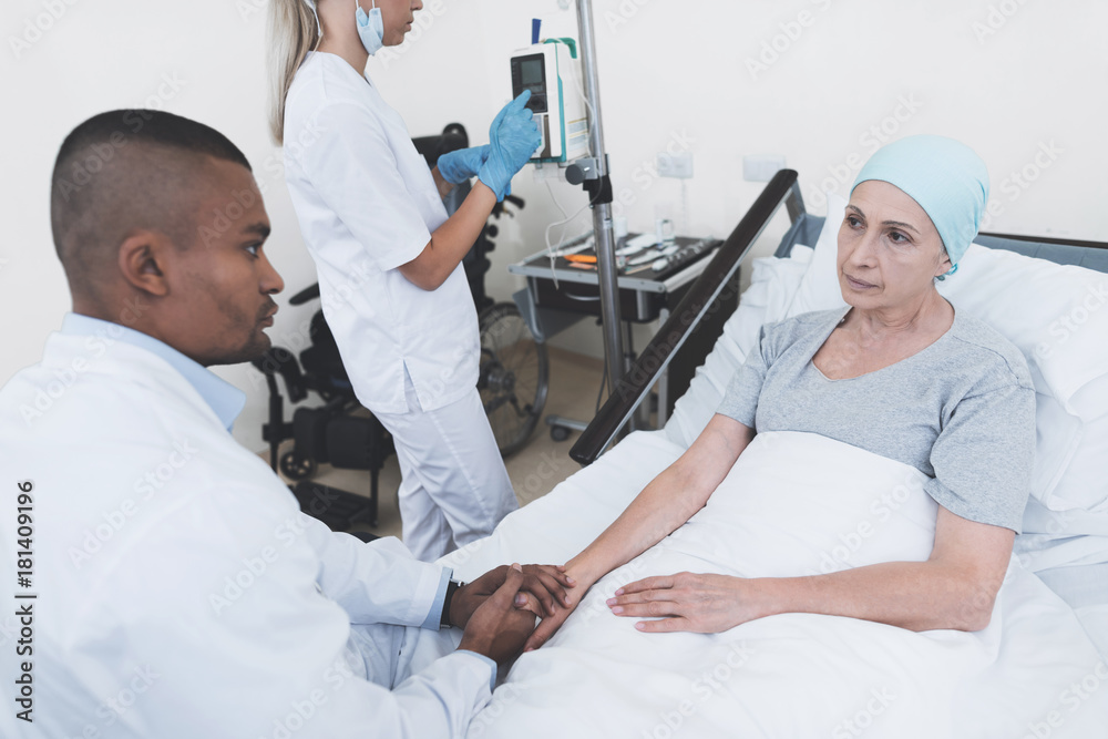 Fototapeta premium The nurse sets the woman a dropper. A doctor is sitting next to him, who is holding a woman with cancer by the hand.