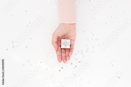 Small Silver Gift Box in female palm. White holiday background with silver tinsel. Presenting or Receiving a gift concept. Top view.