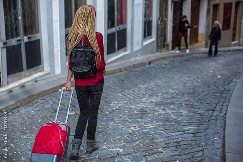 The girl is on the pavement with a red suitcase.