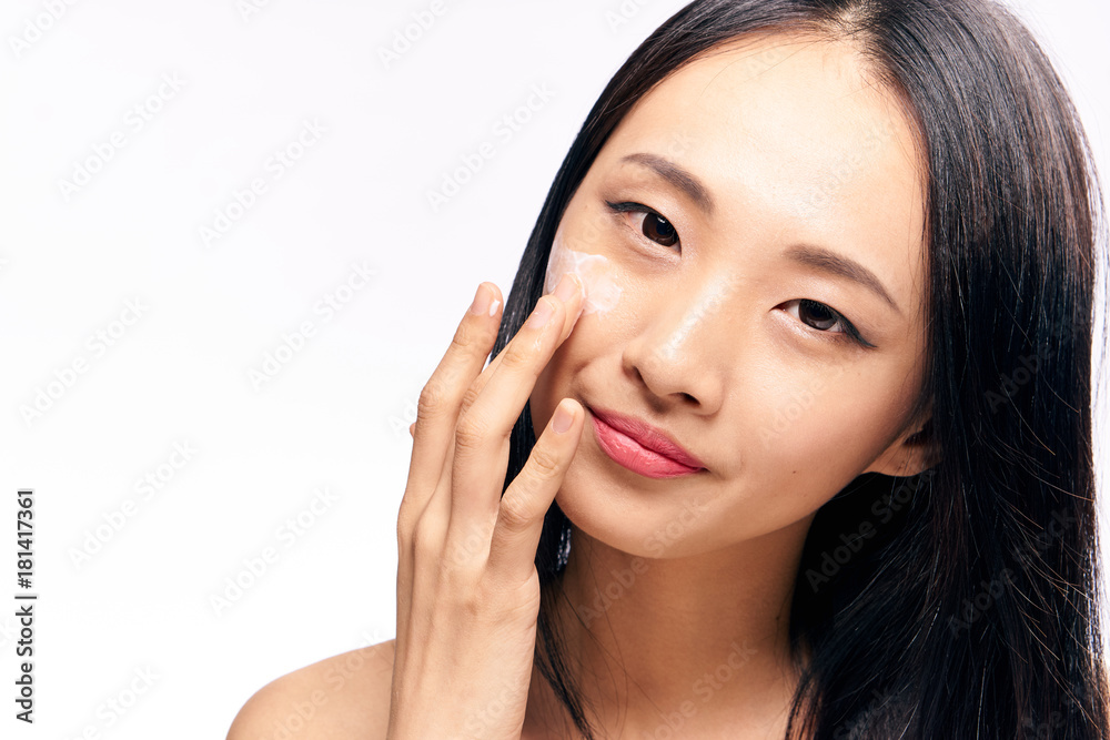 Asian, woman on white isolated background applies cosmetic face cream
