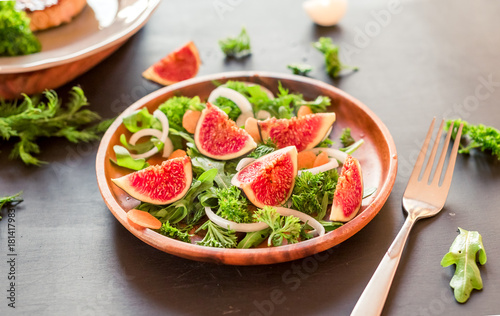 Autumn salad of arugula, figs in a brown earthenware plate on a dark background. top view