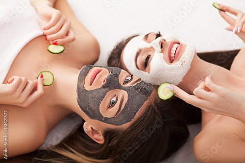 Home spa. Two women holding pieces of cucumber on their faces lying the bed.