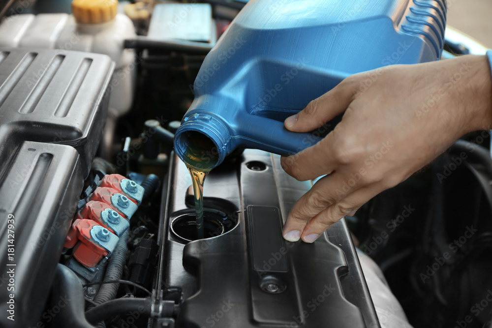 Young male mechanic pouring engine oil from canister, closeup Young male mechanic pouring engine oil from canister, closeup