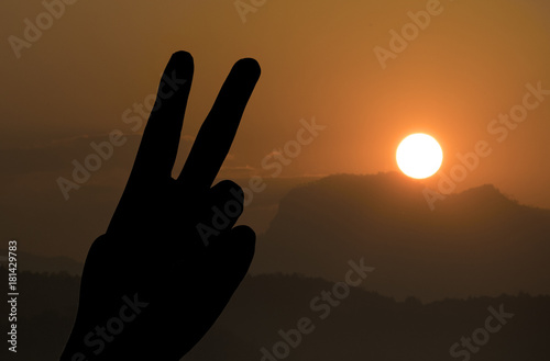 Silhouette of two fingers of woman’s hand or victory sign on the mountain landscape during sunset, number two