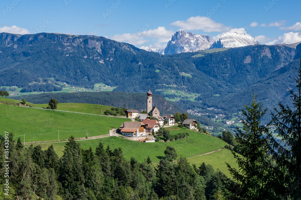 View Alpine village with church and buildings at summer day, Dolomites mountains background.  Soprabolzano, Oberbozen, South Tirol, Italy.