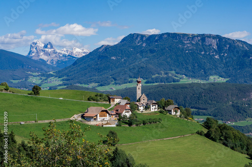 View Alpine village with church and buildings at summer day, Dolomites mountains background.  Soprabolzano, Oberbozen, South Tirol, Italy.
