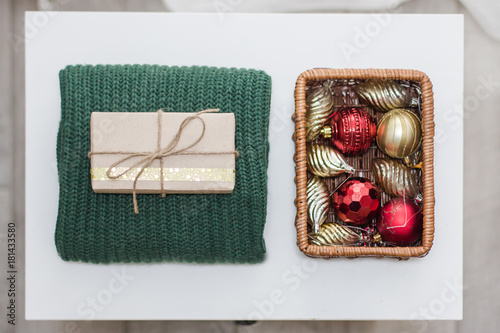 Preparation for the new year. Christmas toys in a basket, folded sweater, gift in a package on a white background.