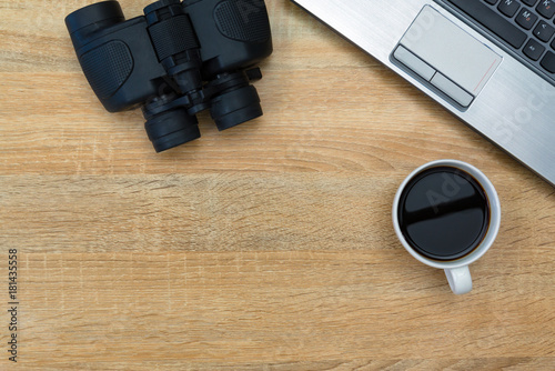 Laptop computer or notebook and binocular, calculator and cup of coffee on working table with copy space top view.