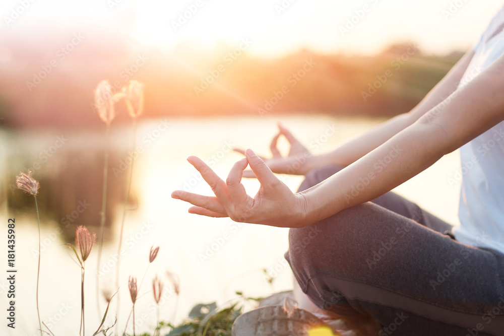 Fototapeta premium Woman practicing yoga and meditating by the lake in summer background