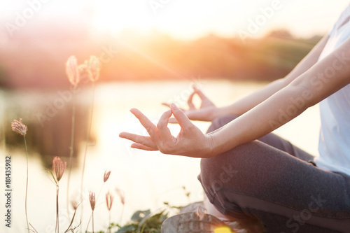 Woman practicing yoga and meditating by the lake in summer background