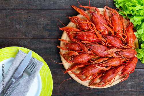 A pile of tasty boiled crawfish on a round wooden tray on a dark table. Top view. Free space for an inscription.