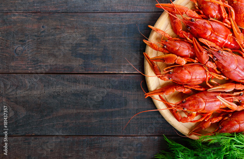 A  pile of tasty boiled crawfish on a round wooden tray on a dark table. Top view. Free space for an inscription.