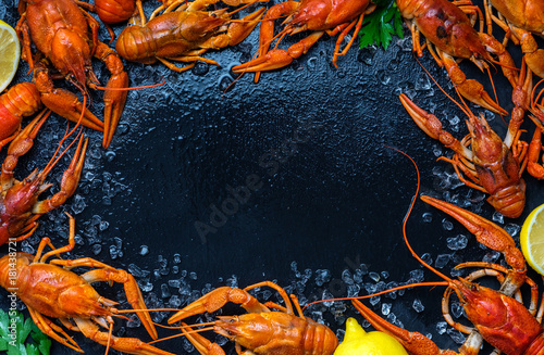 Fresh boiled crawfish with lemons and greens on a dark table with ice