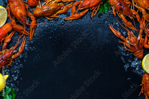 Fresh boiled crawfish with lemons and greens on a dark table with ice