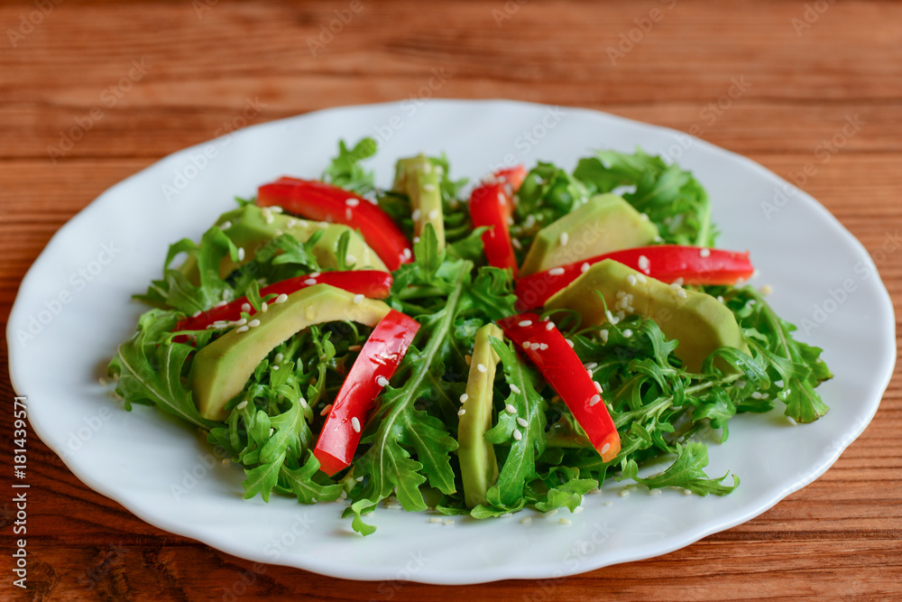 Avocado, arugula and pepper salad on a white plate. Simple arugula and avocado salad with red pepper and sesame seeds. Raw food menu. Closeup