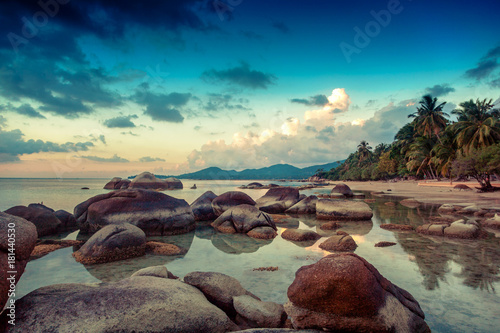 Sea shore at sunset with large stones and reflection of clouds in the water. Beautiful tropical landscape