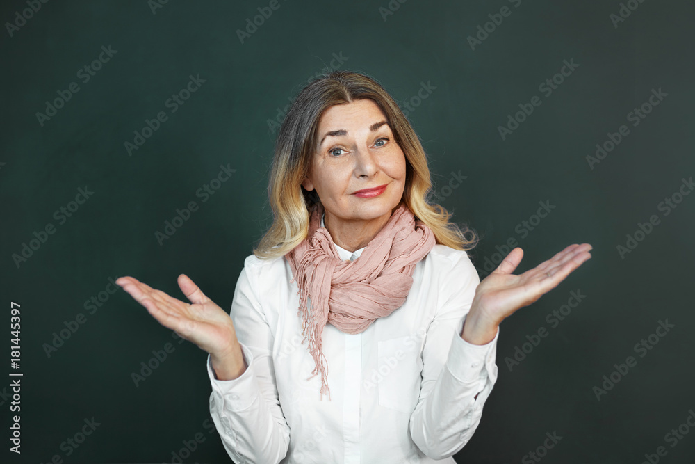 Positive beautiful middle aged European female with charming smile raising hands as if making scale with her arms wide open. Confused senior woman feeling uncertain, shrugging her shoulders Positive beautiful middle aged European female with charming smile raising hands as if making scale with her arms wide open. Confused senior woman feeling uncertain, shrugging her shoulders
