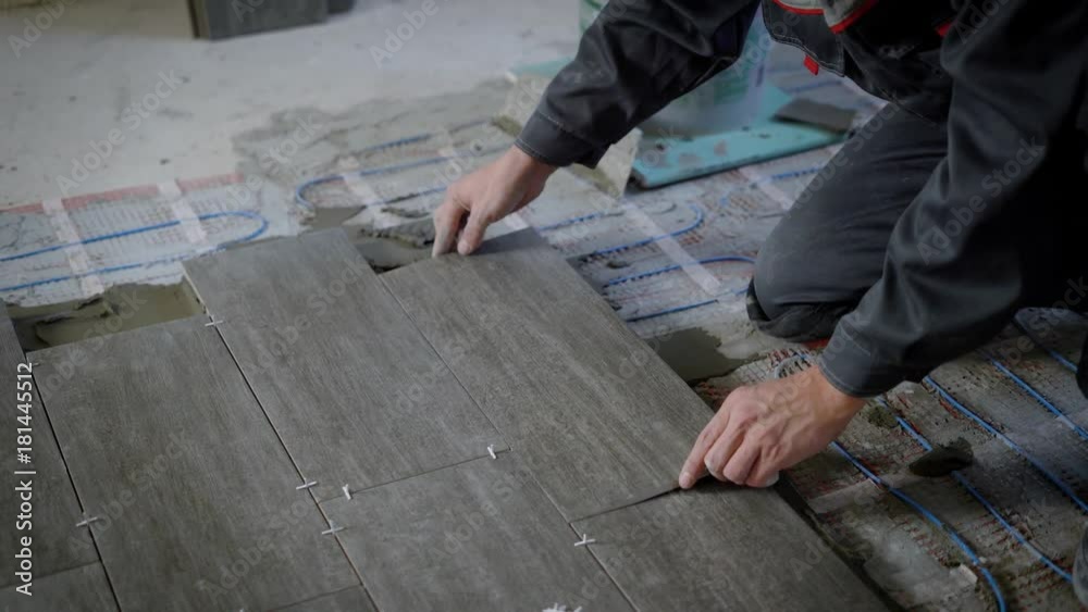 tiler is lying tile on a floor, pressing down and regulating, installing plastic industrial crosses for fixing tiler is lying tile on a floor, pressing down and regulating, installing plastic industrial crosses for fixing