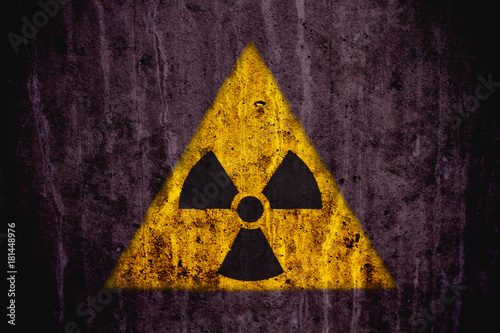 Triangular yellow and black radioactive (ionizing radiation) danger symbol painted on a massive concrete wall with dark rustic grunge texture background.