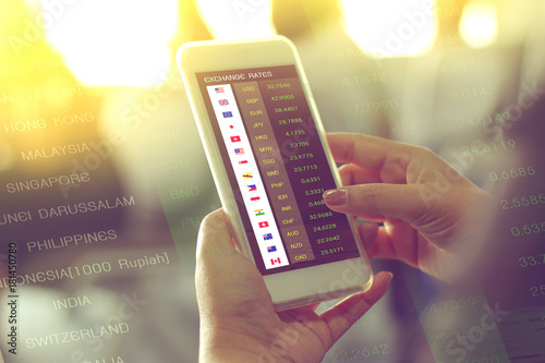 hand holding smartphone for checking exchange rates by currency application on fight to travel, double exposure with currency exchange rates background