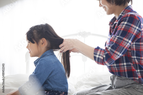 In the bedroom, a young mother is tying her daughter's hair. photo