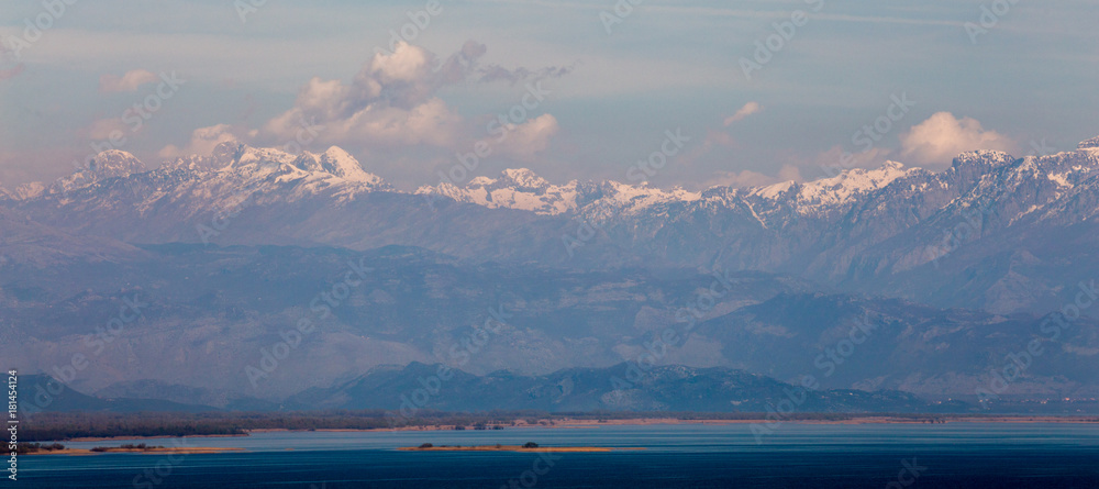 panorama of high mountains with snowy peaks, white clouds and blue water at  foot at dawn
