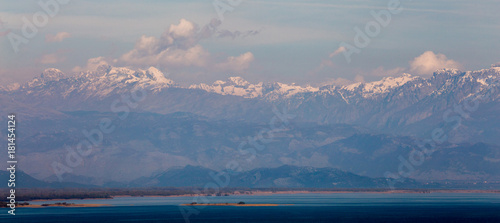 panorama of high mountains with snowy peaks, white clouds and blue water at  foot at dawn © Aleksei Lazukov