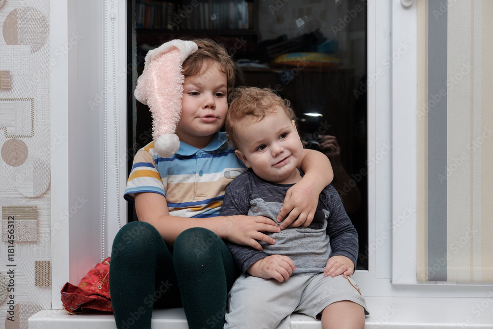 two lovely boy of European appearance sitting on the windowsill two lovely boy of European appearance sitting on the windowsill