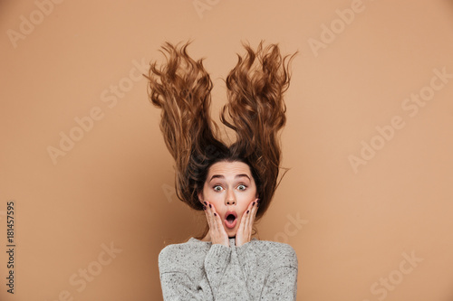 Close-up photo of attractive shocked woman with funny hairstyle touching her face, looking at camera