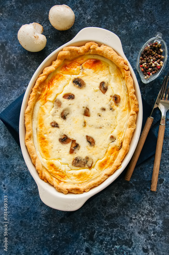 Homemade delicious quiche with mushrooms and cheese in a dish on a blue stone background. Homemade delicious quiche with mushrooms and cheese in a dish on a blue stone background.
