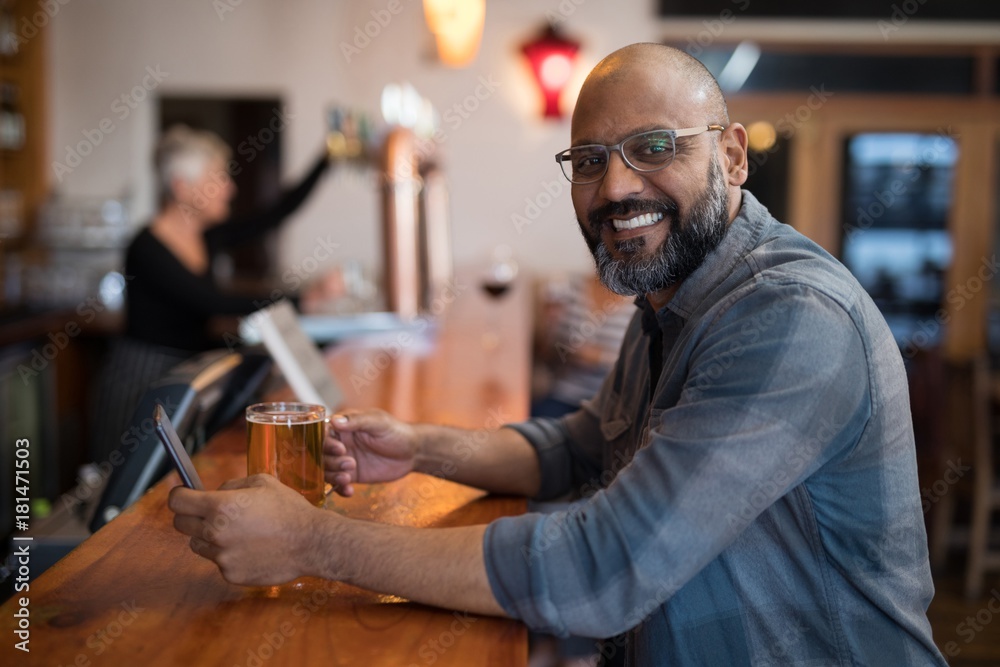 Smiling man using mobile phone while having beer at counter in