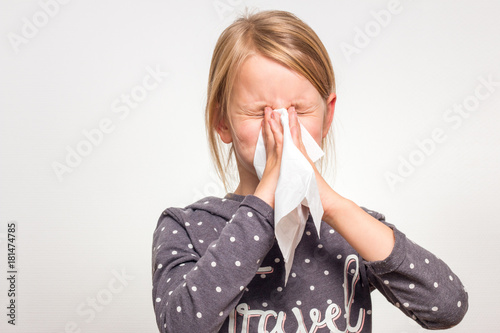 Ein Mädchen schnäuzt in ein weißes Taschentuch. Sie ist 7 Jahre alt und trägt einen grauen weiß gepunkteten Pullover. Freisteller photo