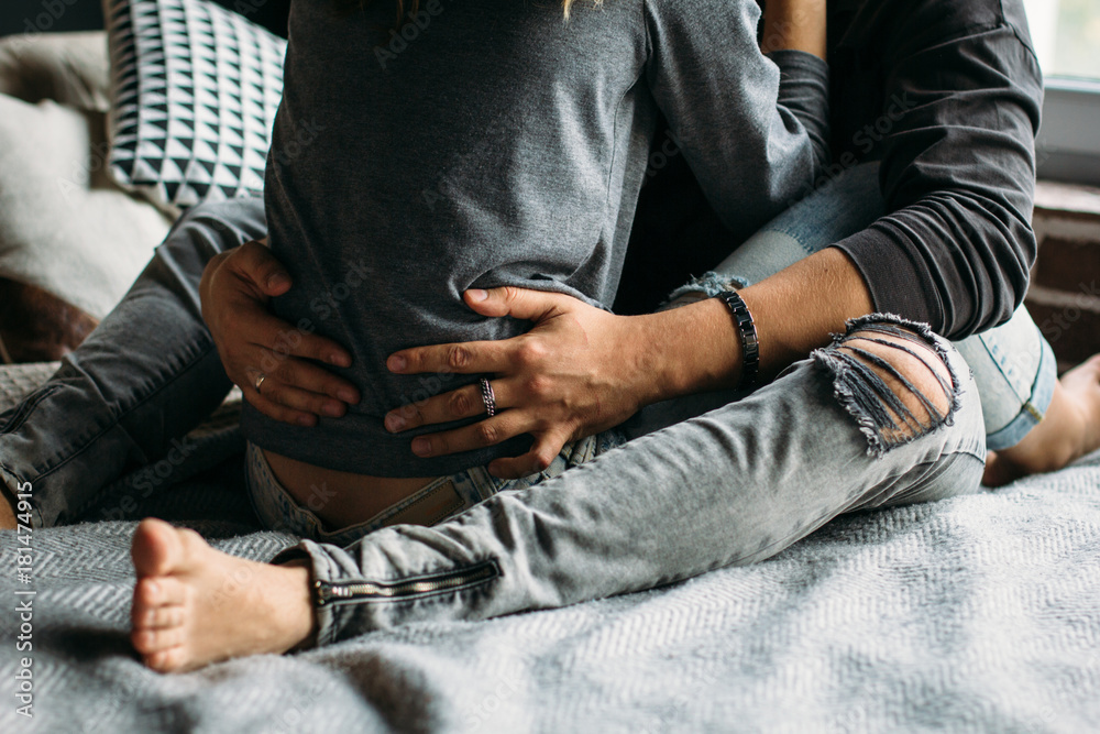 Young beautiful pair of lovers hug and kiss. Cropped image. Legs in grey ragged jeans