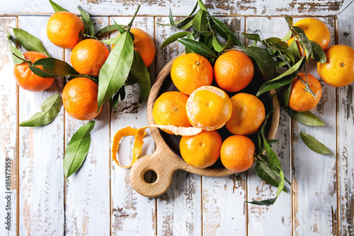 Ripe organic clementines or tangerines with leaves on wood serving board over white wooden plank table as background. Top view, space. Healthy eating