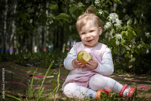 Little girl portrait eating red apple in the park