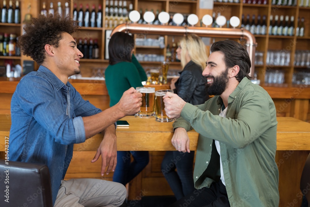 Two friends toasting glass of beer at counter in bar