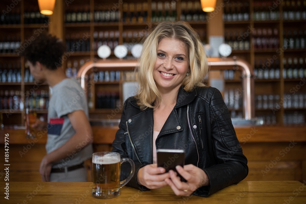 Smiling beautiful woman using mobile phone while having glass of