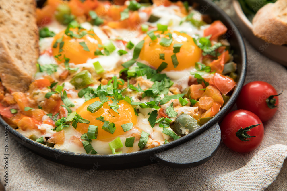 Shakshuka with eggs, tomato, and parsley in a iron pan. Shakshuka - traditional israeli tomato stew with eggs Shakshuka with eggs, tomato, and parsley in a iron pan. Shakshuka - traditional israeli tomato stew with eggs