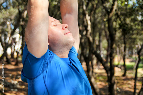 Fototapeta Naklejka Na Ścianę i Meble -  Handsome young man is doing stretching exercises in forest. Sportsman wearing sportswear in landscape nature outdoors. Pretty guy, active, cross fit, healthy lifestyle, fitness relax people concept.
