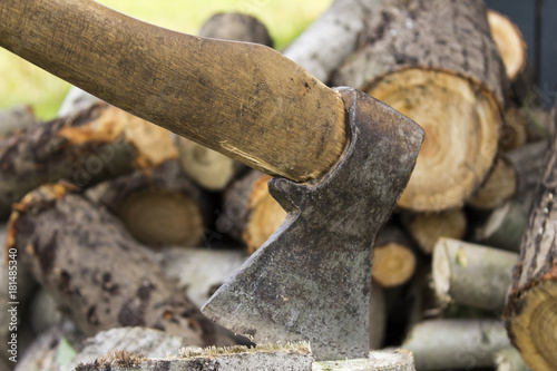 An ax stuck in a stump. A woodpile. Background
