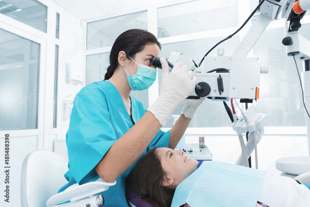 Fototapeta premium A female dentist is treating a girl. She sits on the dental chair and smiles.