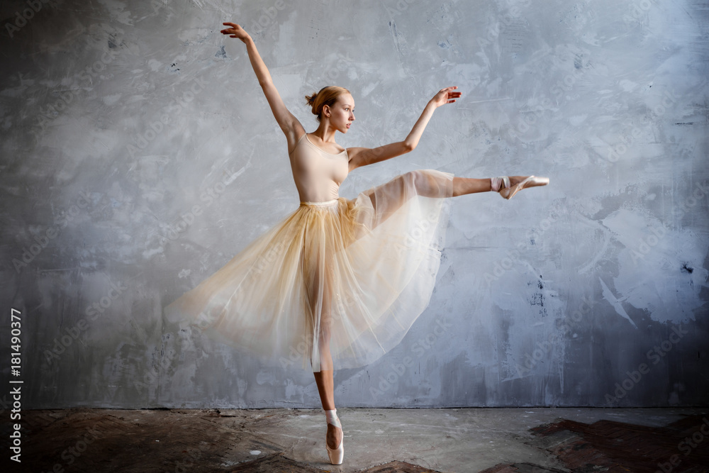Fototapeta premium Young ballerina in a golden colored dancing costume is posing in a loft studio